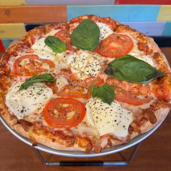 A TJ's Burgers, Wings, and Pizza Margherita pizza with fresh basil, mozzarella, and sliced tomatoes.