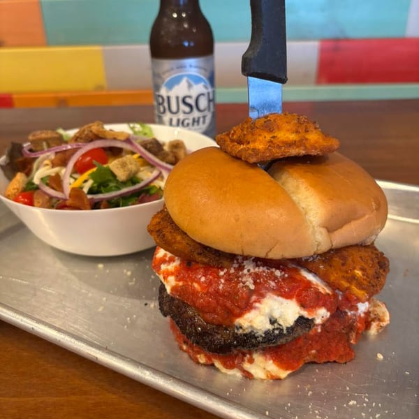 TJ's Burgers' burger with red sauce, cheese, and fried toppings, served with a salad and Busch Light.